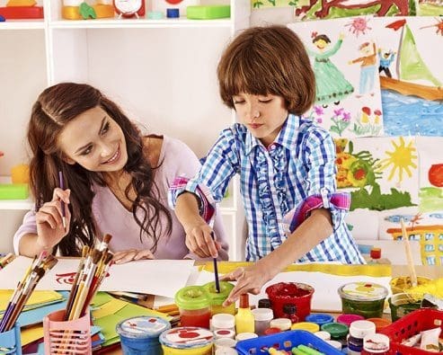 maestra y estudiante a una mesa con pinturas