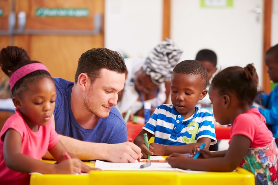 Maestro dibujando a una mesa con niños Maestro sentándose con niños pequeños en un aula