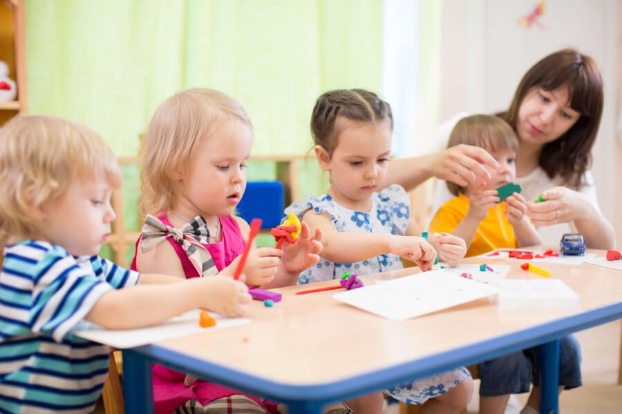 Children and a woman playing with play dough at a table Children and a woman playing with play dough at a table
