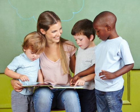 maestra mirando un libro con 3 niños