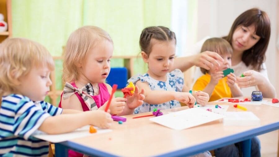 Children and a woman playing with play dough at a table