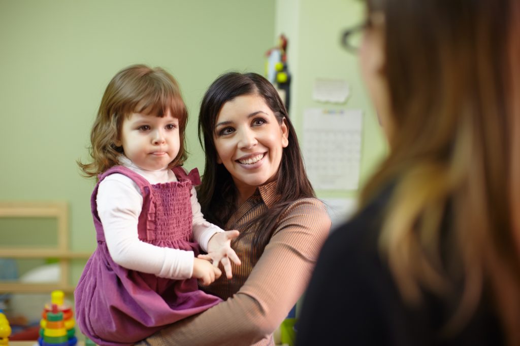 Mother holding her daughter and facing child care provider