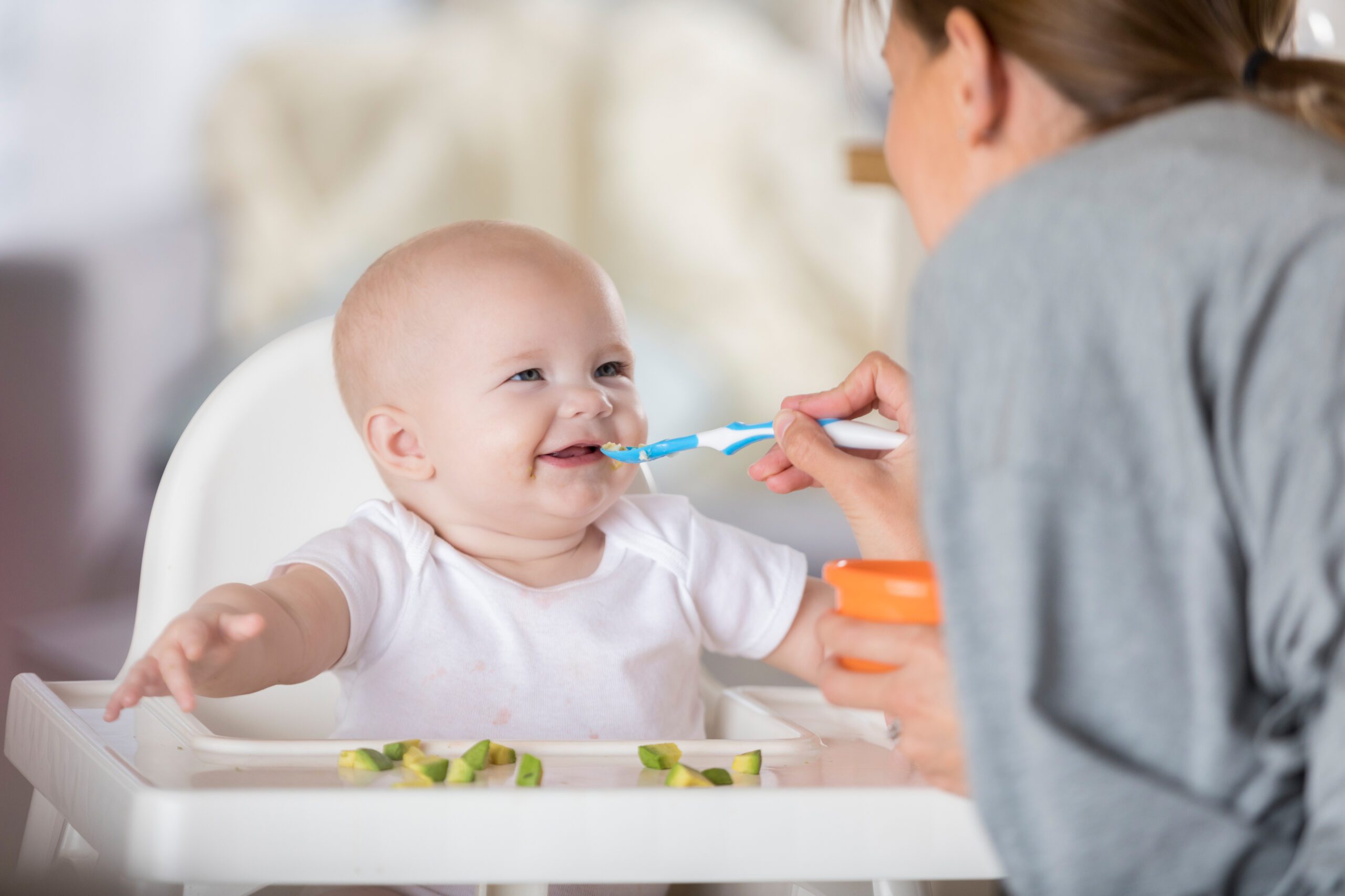 Adorable baby in high chair laughs while being spoon fed
