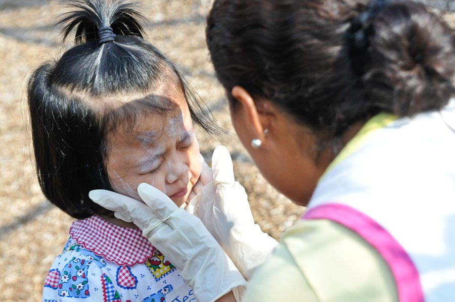 child care provider applies sunscreen to young girl outside