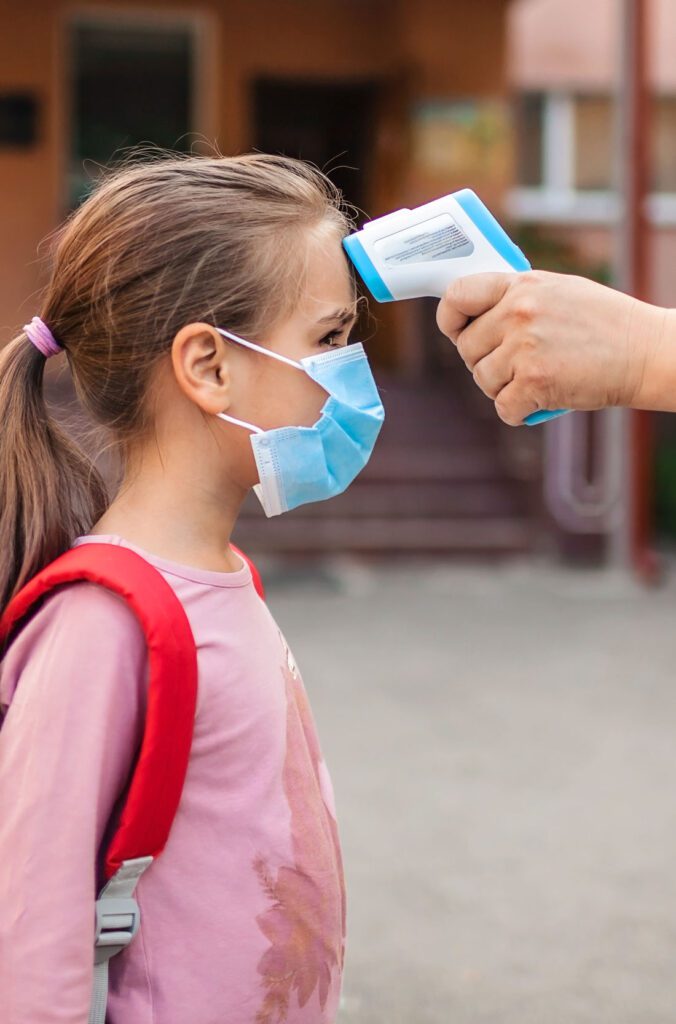 girl gets her temperature taken before entering school building