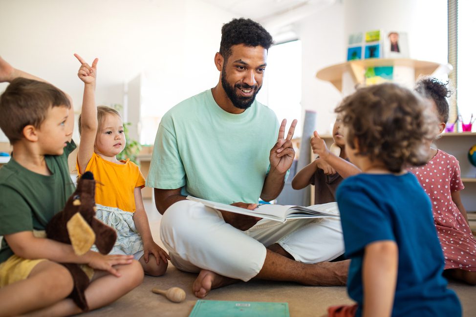 Group,Of,Small,Nursery,School,Children,With,Man,Teacher,Sitting